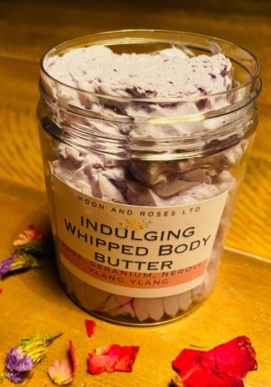 A pot of indulging whipped body butter with rose petals surrounding it