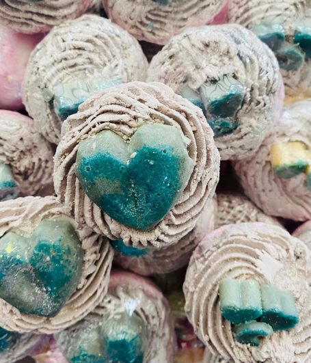 a pile of relaxing bath bombs focused in on one at the top, with a large blue shiny heart on grey rippled icing